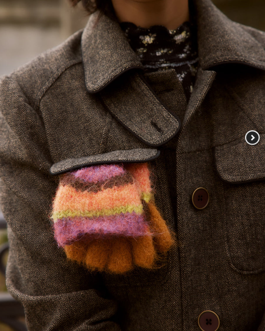 model carrying orange, pink, green and brown striped gloves/mittens in their pocket