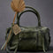 olive green leather bag with two sets of straps and various zippers and zipper pulls