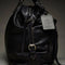 side view of black leather purse with several zippered pockets, double handles and crossbody strap