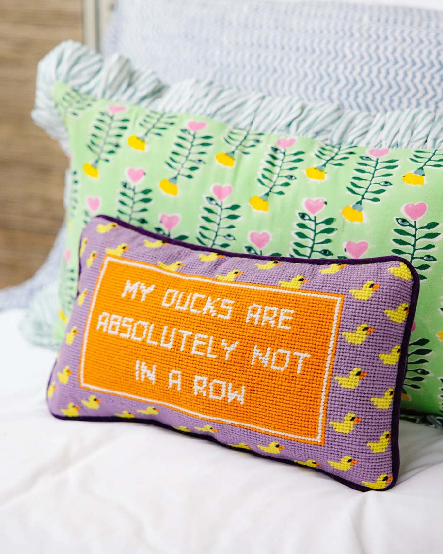 purple throw pillow with duck border and 'my ducks are absolutely not in a row' across the front on a bed