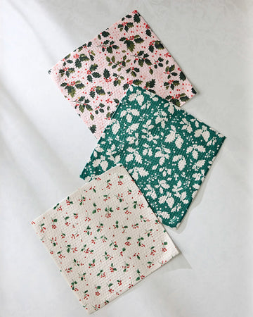 set of three holiday dish cloths: pink with holly print, green with shadow holly print, and white with dainty sprig print