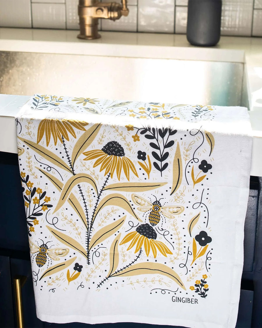 white tea towel with goldenrod floral and bee print folded on a sink