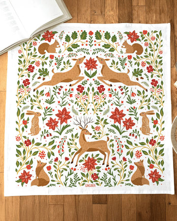 white tea towel with all over poinsettia, deer, rabbit, and fox print