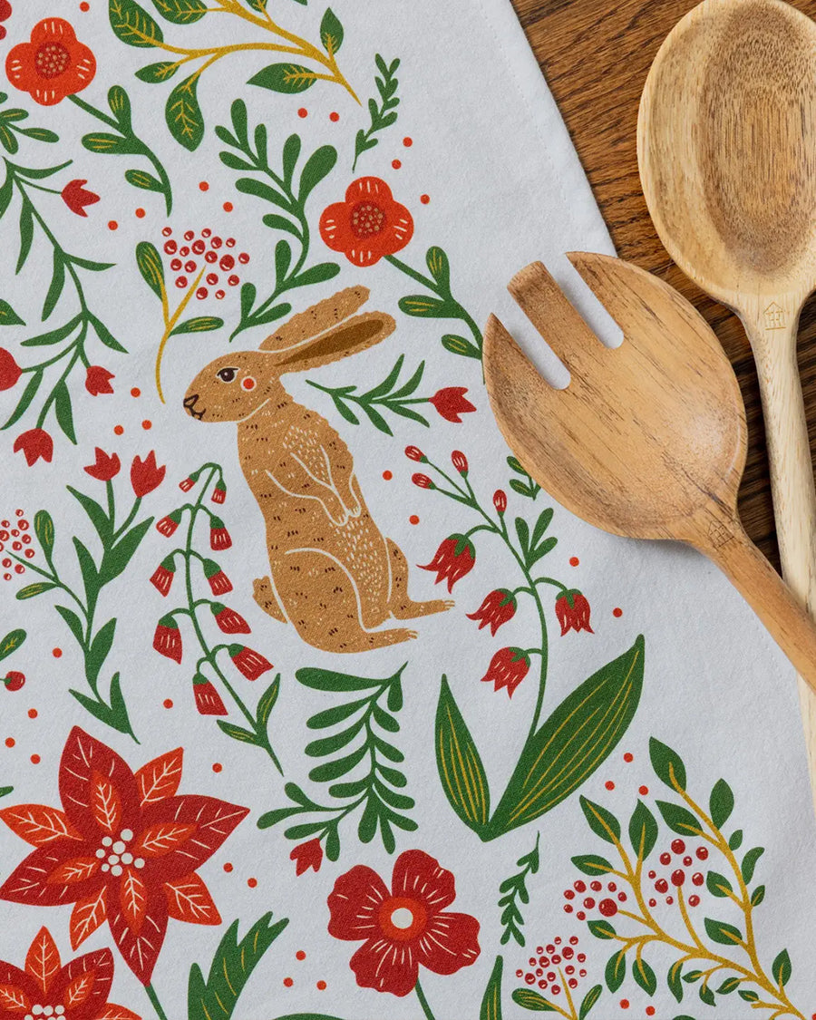 up close of white tea towel with all over poinsettia, deer, rabbit, and fox print