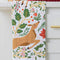 folded white tea towel with all over poinsettia, deer, rabbit, and fox print