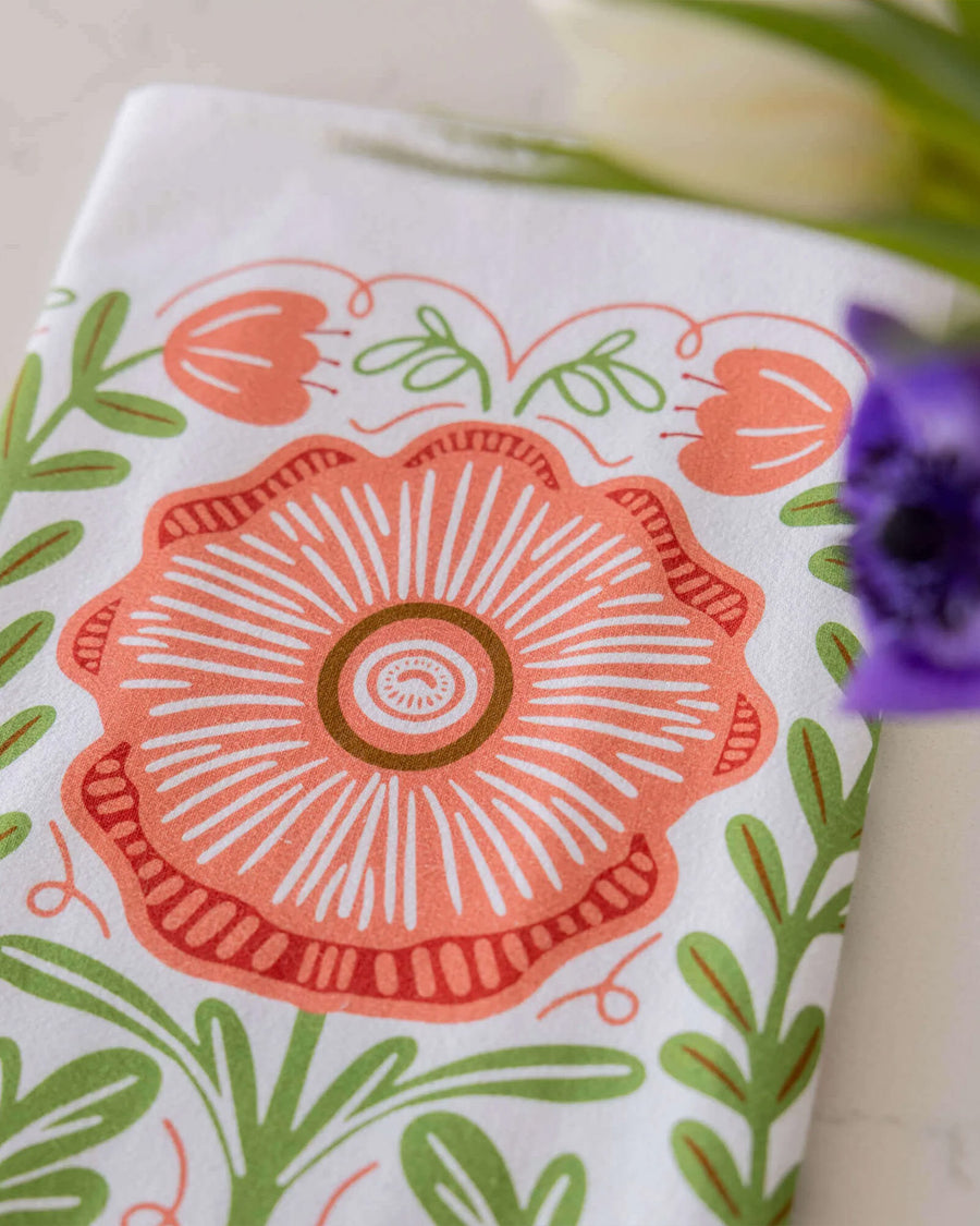 top view of white tea towel with abstract pink poppy print and greenery