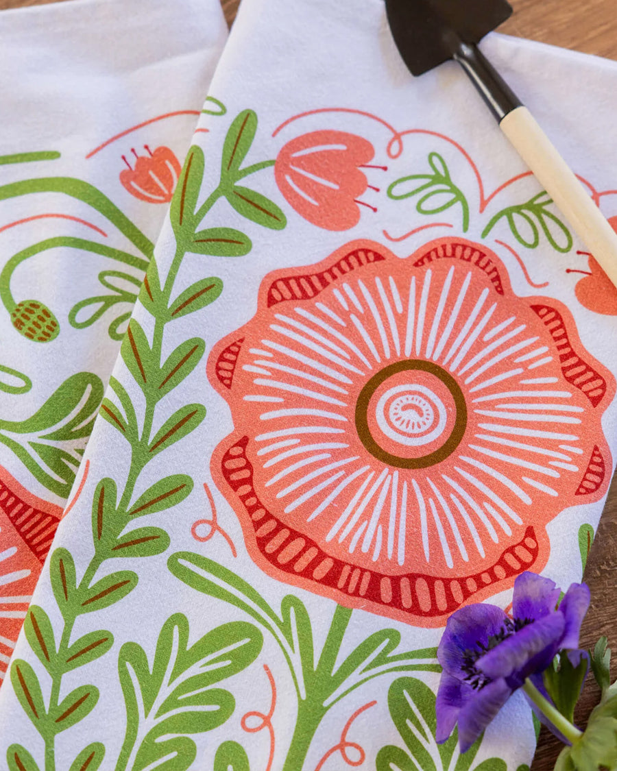 up close of white tea towel with abstract pink poppy print and greenery