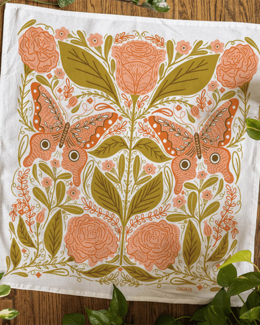 white tea towel with pink butterfly moth print and green leaves on a table