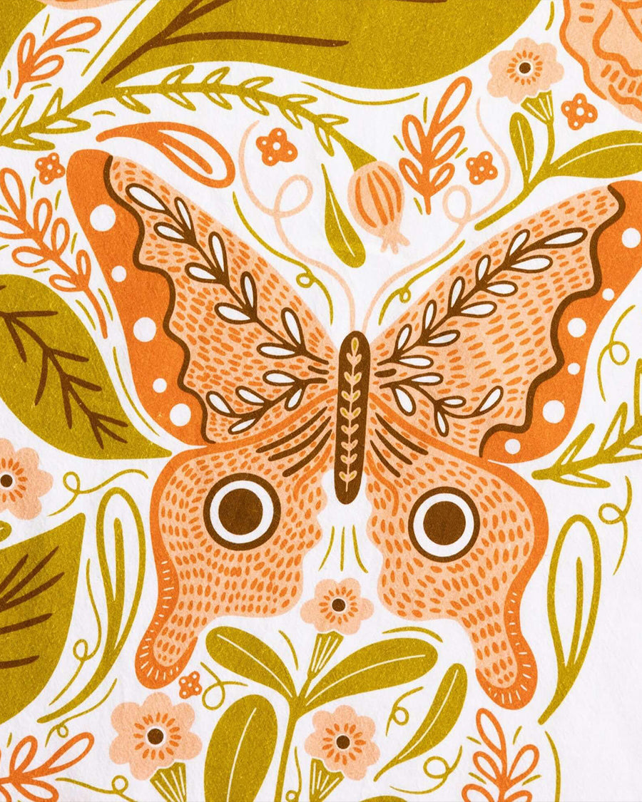 up close of white tea towel with pink butterfly moth print and green leaves
