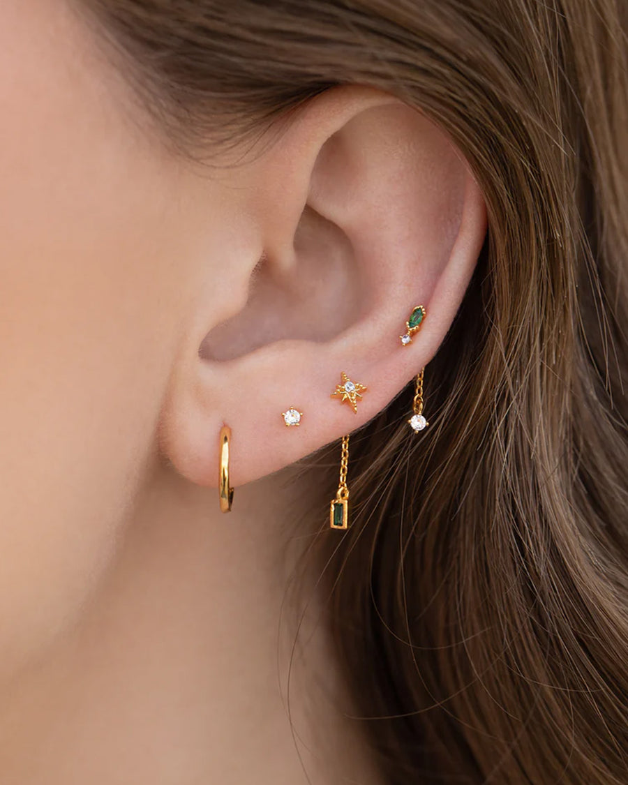 model wearing set of 5 gold mismatched earrings  with clear crystal and emerald stone accents