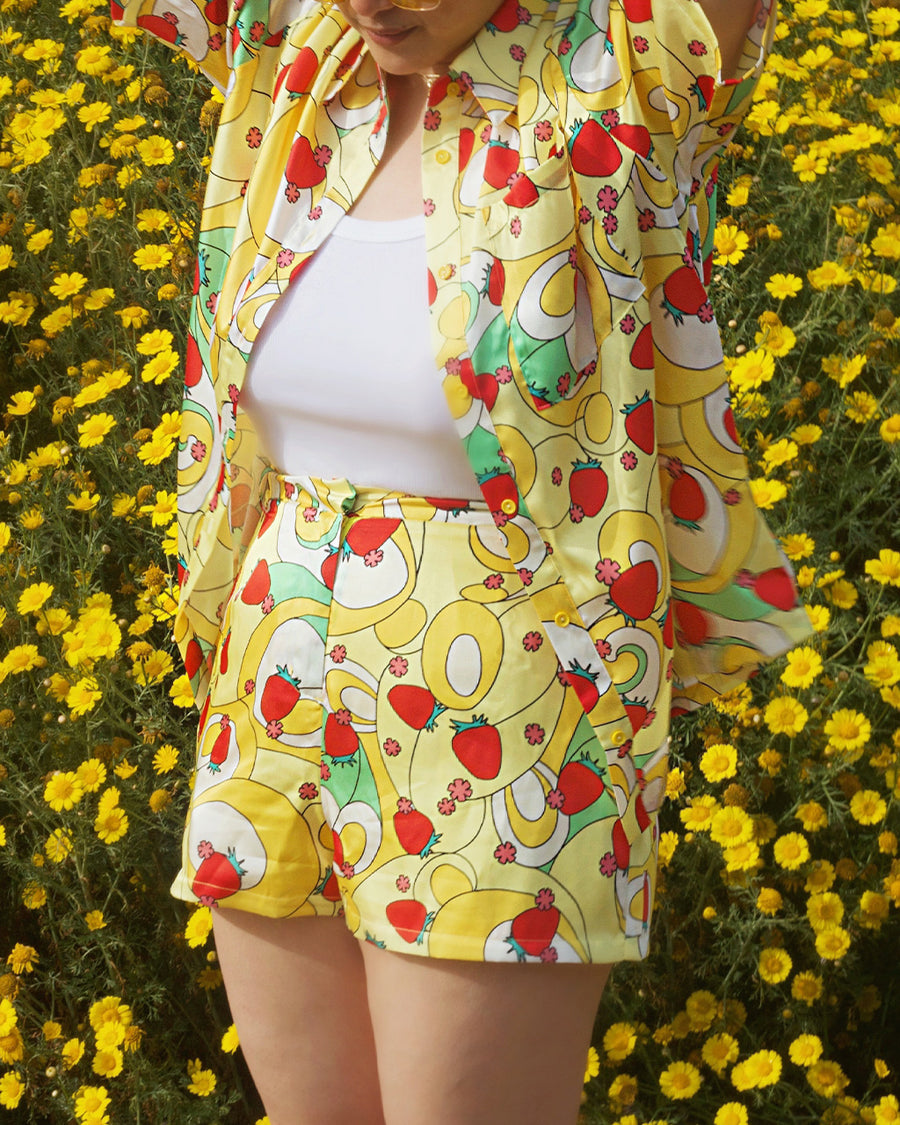 model wearing yellow trippy shorts with vibrant strawberry and flower print and paired with matching button down top