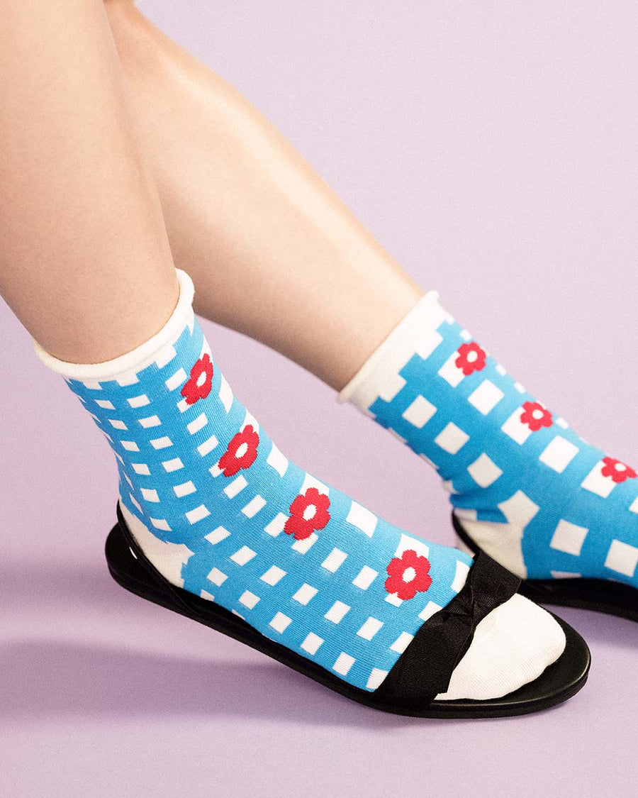 up close of model wearing blue and white plaid crew socks with red floral print