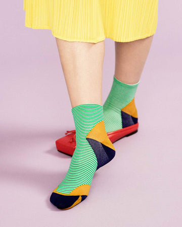 up close of model wearing green and white striped crew socks with orange and black geometric heel