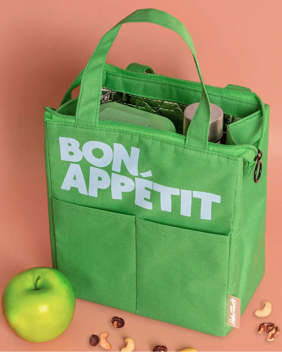kelly green lunch bag with light blue 'bon appetit' across the front on a peach background