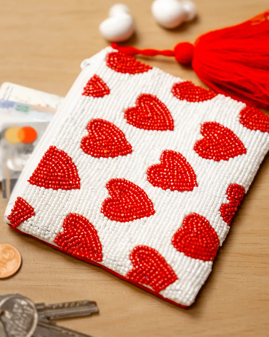 white small beaded clutch with red tassel and red beaded heart design surrounded by change, keys and earbuds