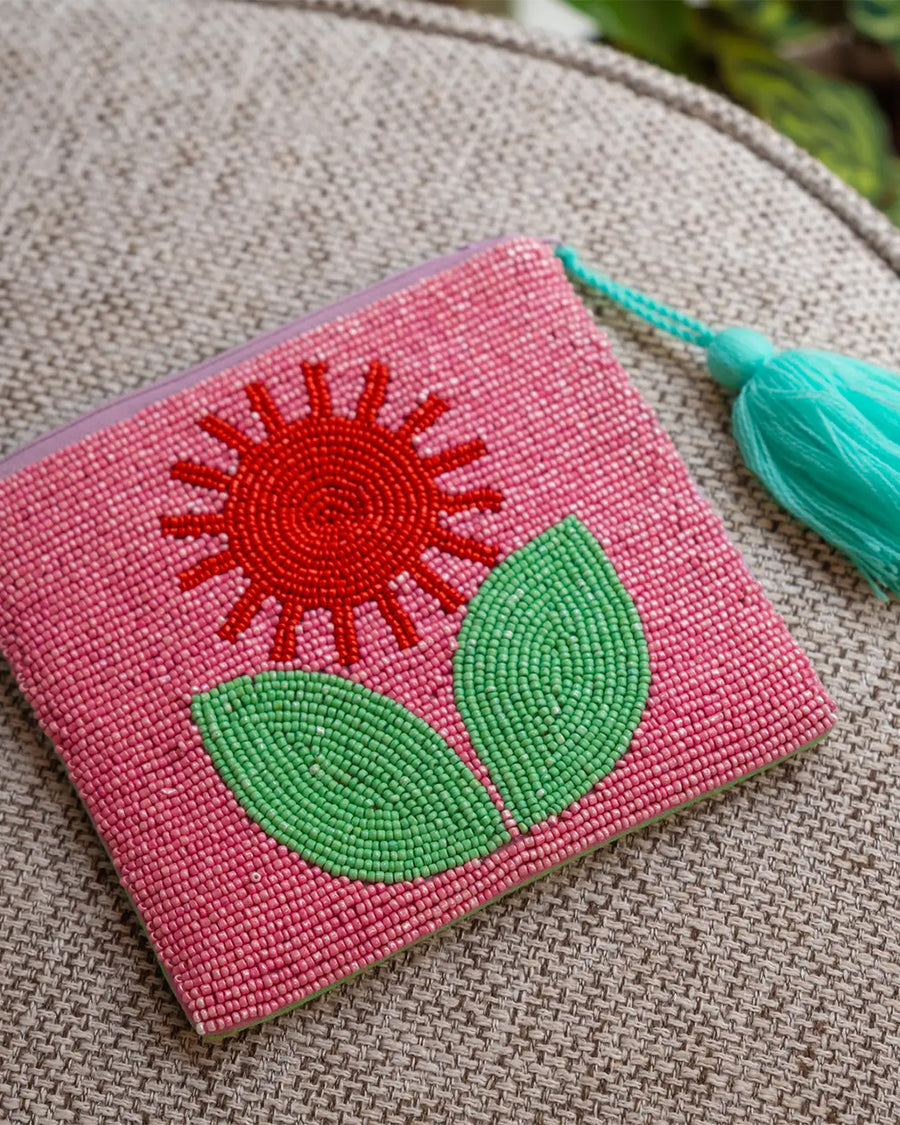 small beaded pink clutch with red and green beaded flower and teal tassel on a table