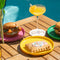 pink, yellow and green plates in an outdoor setting with various breakfast foods on them