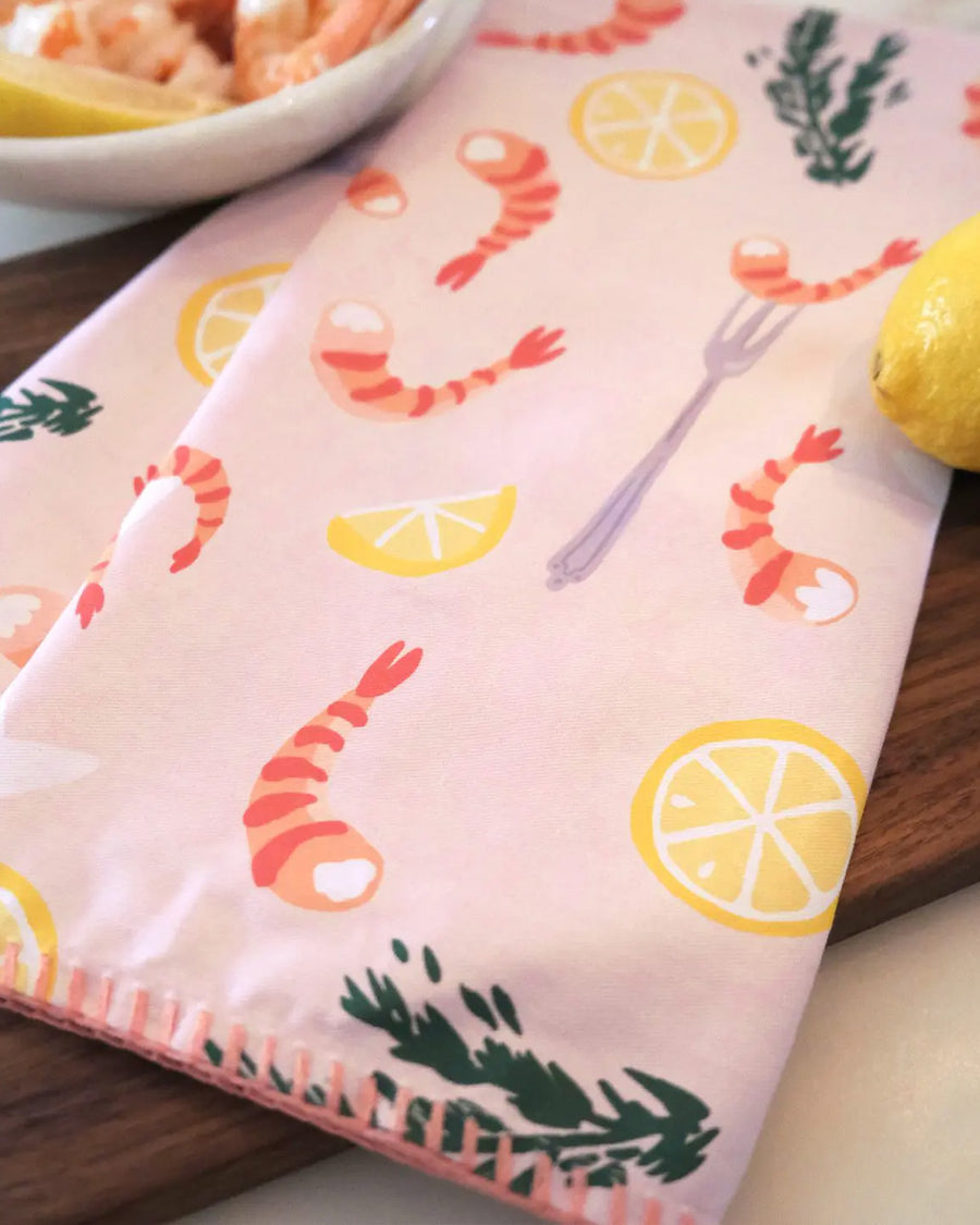 side view of light pink cotton tea towel with shrimp cocktail and lemon print