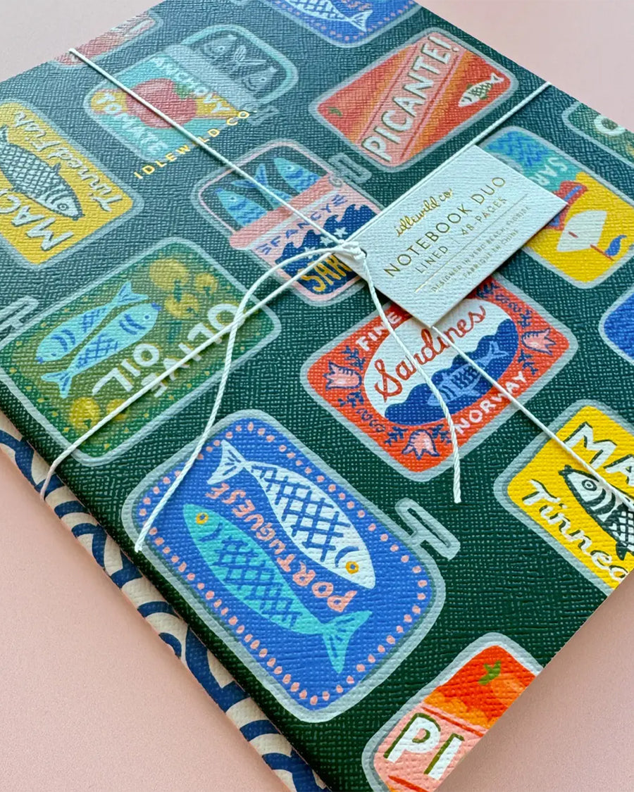 packaged set of 2 notebooks with green with colorful tinned fish print and blue and white arch print