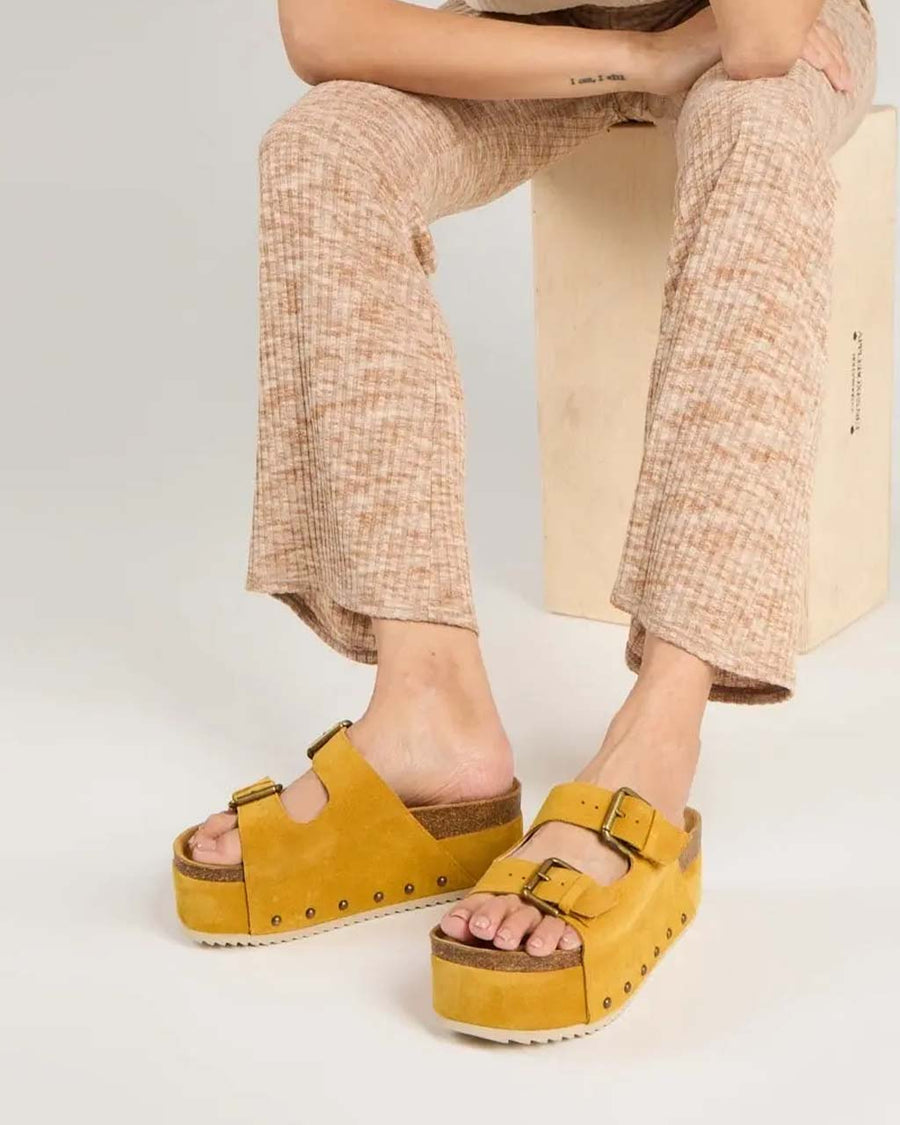 model wearing marigold platform shoes with two buckle straps and grommet details on the sides