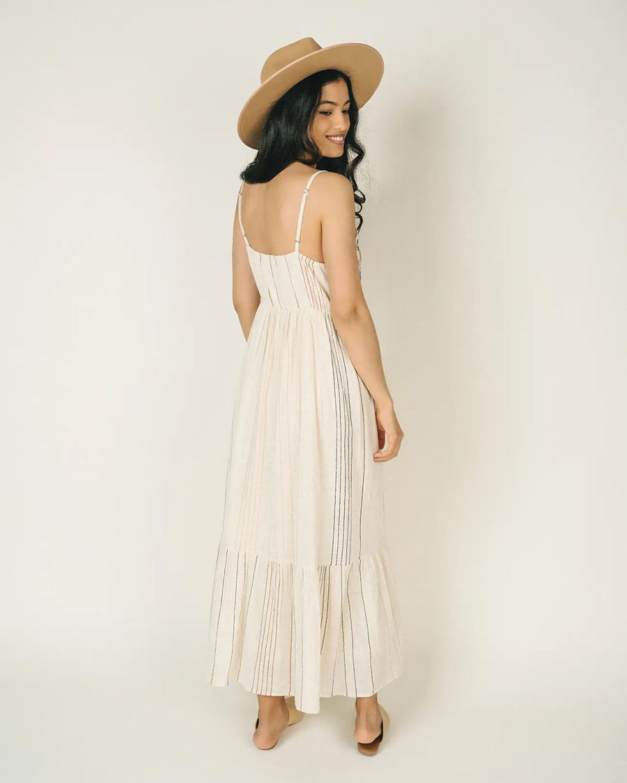 backview of model wearing white maxi dress with pink flower bodice and vertical line detail throughout the dress