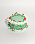 green fake cake kit with white piped 'frosting' and red and white mushrooms