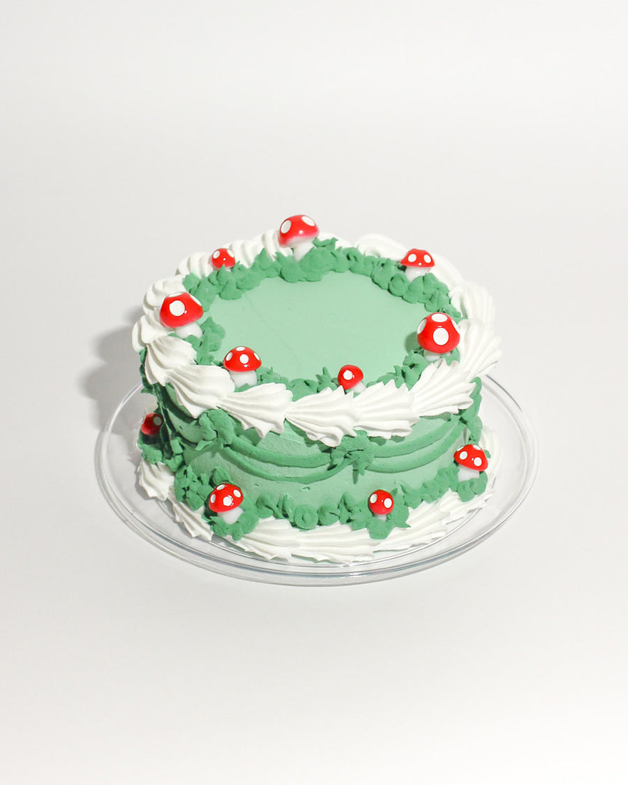 green fake cake kit with white piped 'frosting' and red and white mushrooms on plate
