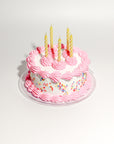 white fake cake kit with pink 'frosting', colorful faux sprinkles and yellow candles on plate