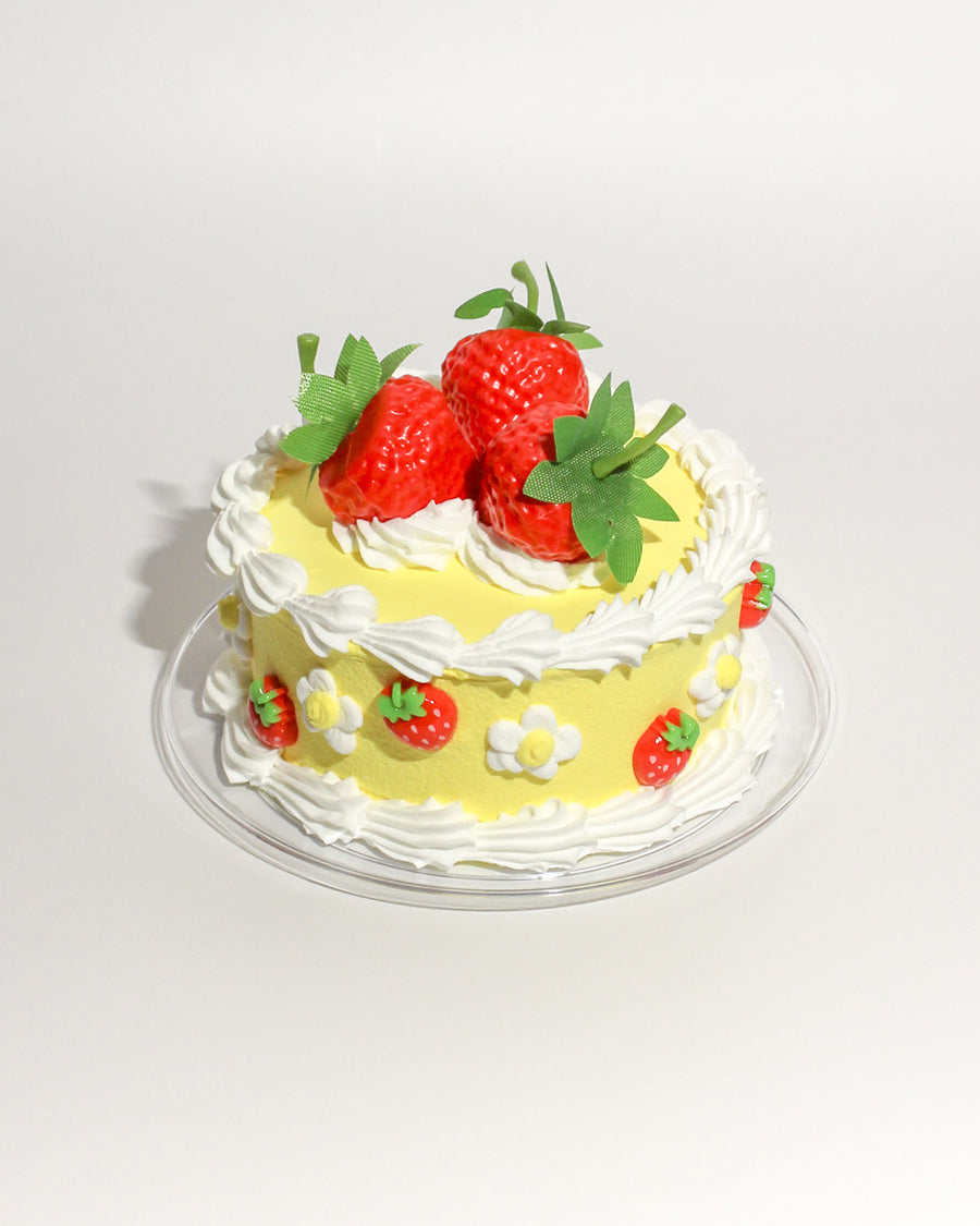 yellow fake cake kit with white 'frosting' and faux strawberries on plate