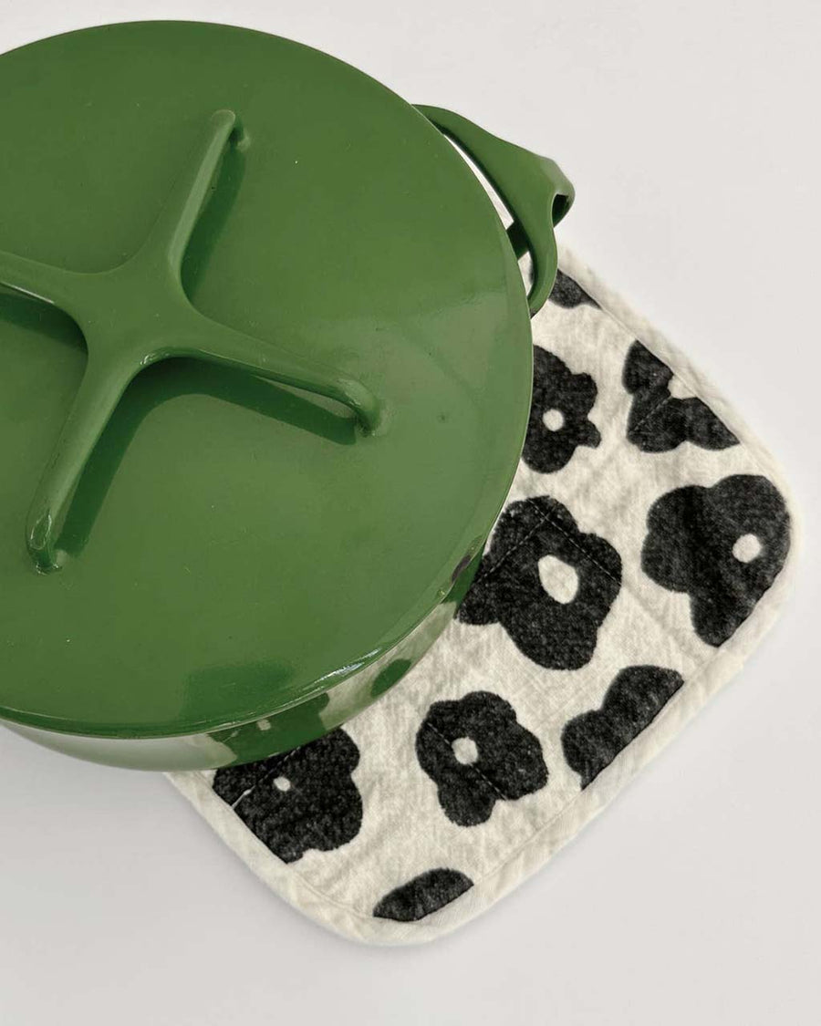 cream potholder with black floral print with green pot on it