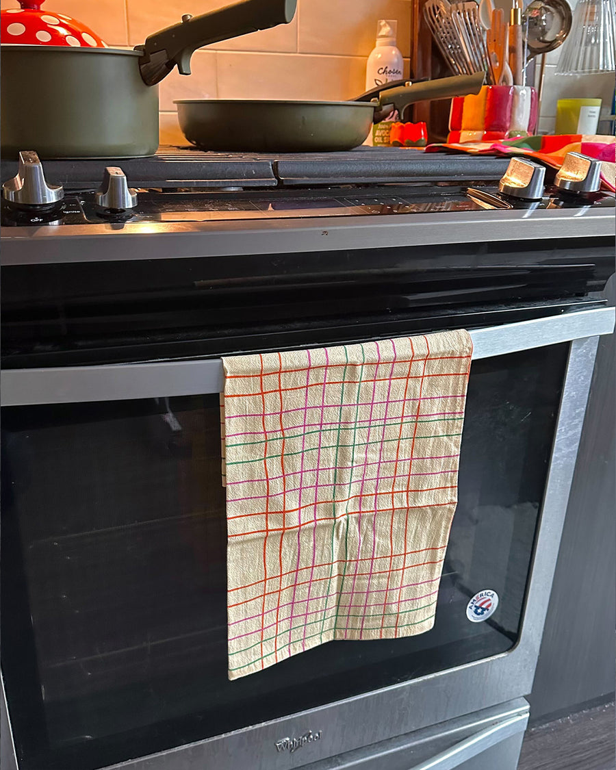 cream tea towel with colorful thin plaid print hanging on an oven handle