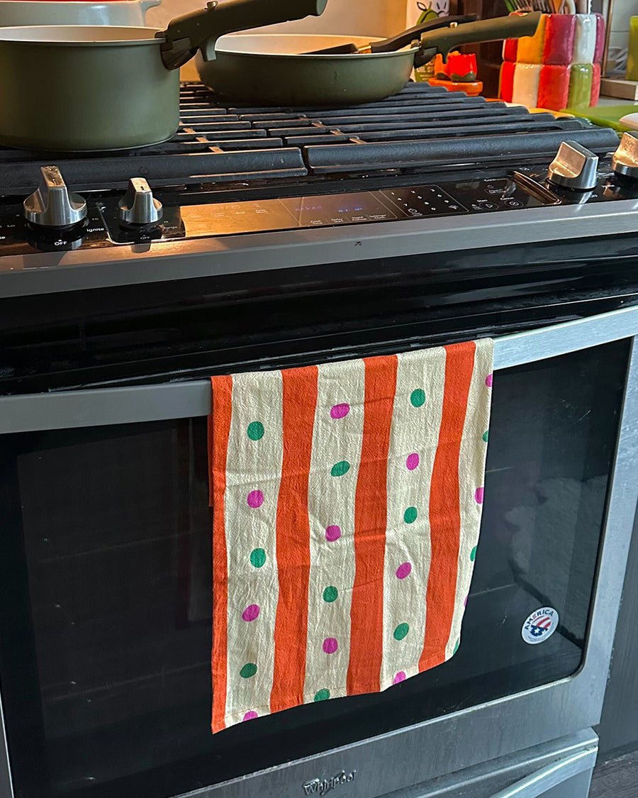 pale yellow and orange striped tea towel with green and pink dots on an oven handle