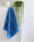 blue cotton tea towel with all over sardine print next to a plant