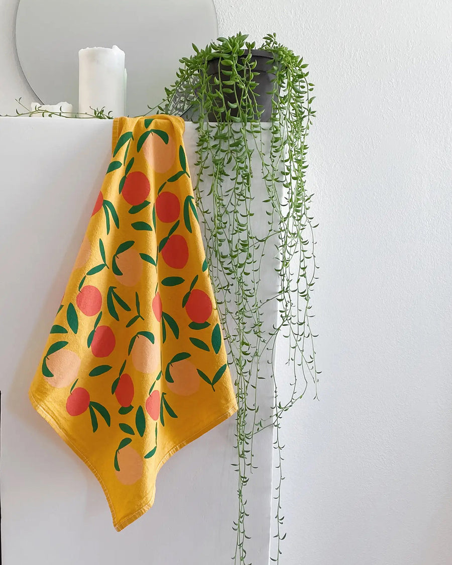 yellow cotton tea towel with all over peach print on a shelf