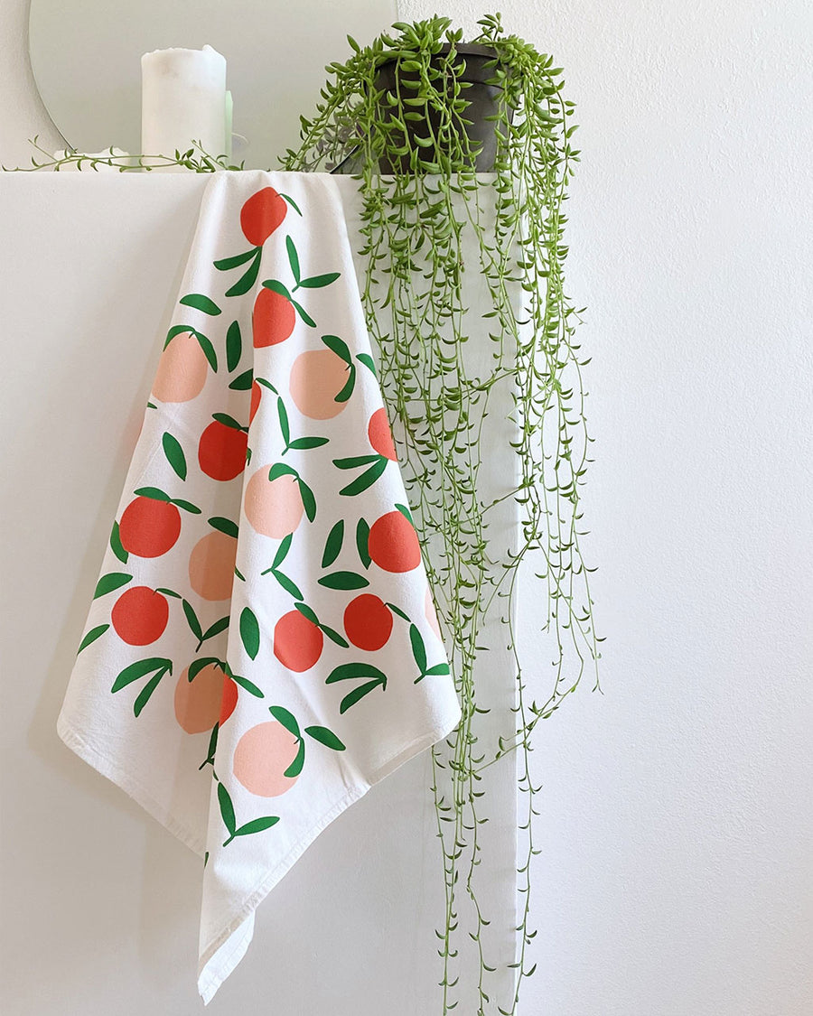 white square tea towel with all over peach print hanging on a shelf