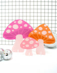 set of three acrylic mushrooms in hot pink, peachy orange and light pink in front of grid wallpaper