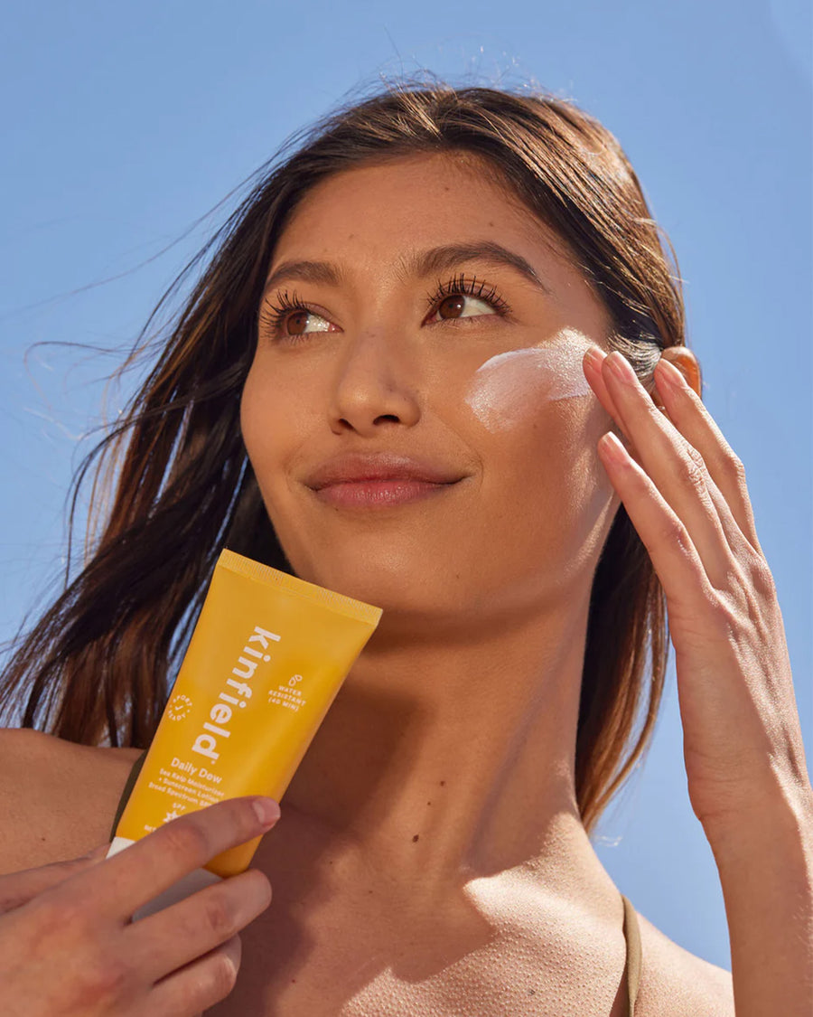 model putting kinfield daily dew sunscreen on her face