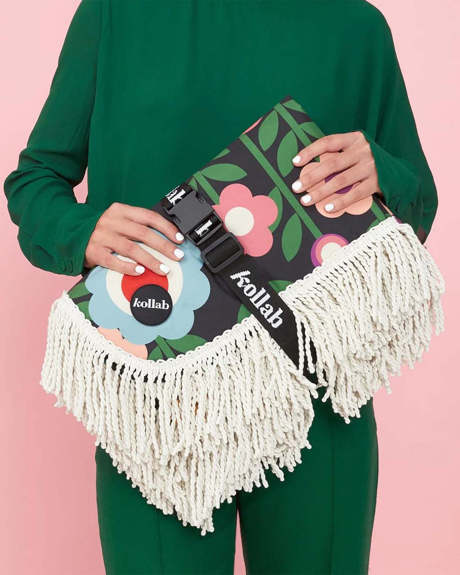 model holding folded medium foldable picnic mat with colorful mod inspired floral print and white fringe