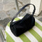 black nylon barrel handbag with leather buckle shoulder strap and trim sitting on a chair