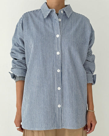 model wearing blue and white vertical pinstripe denim button up shirt