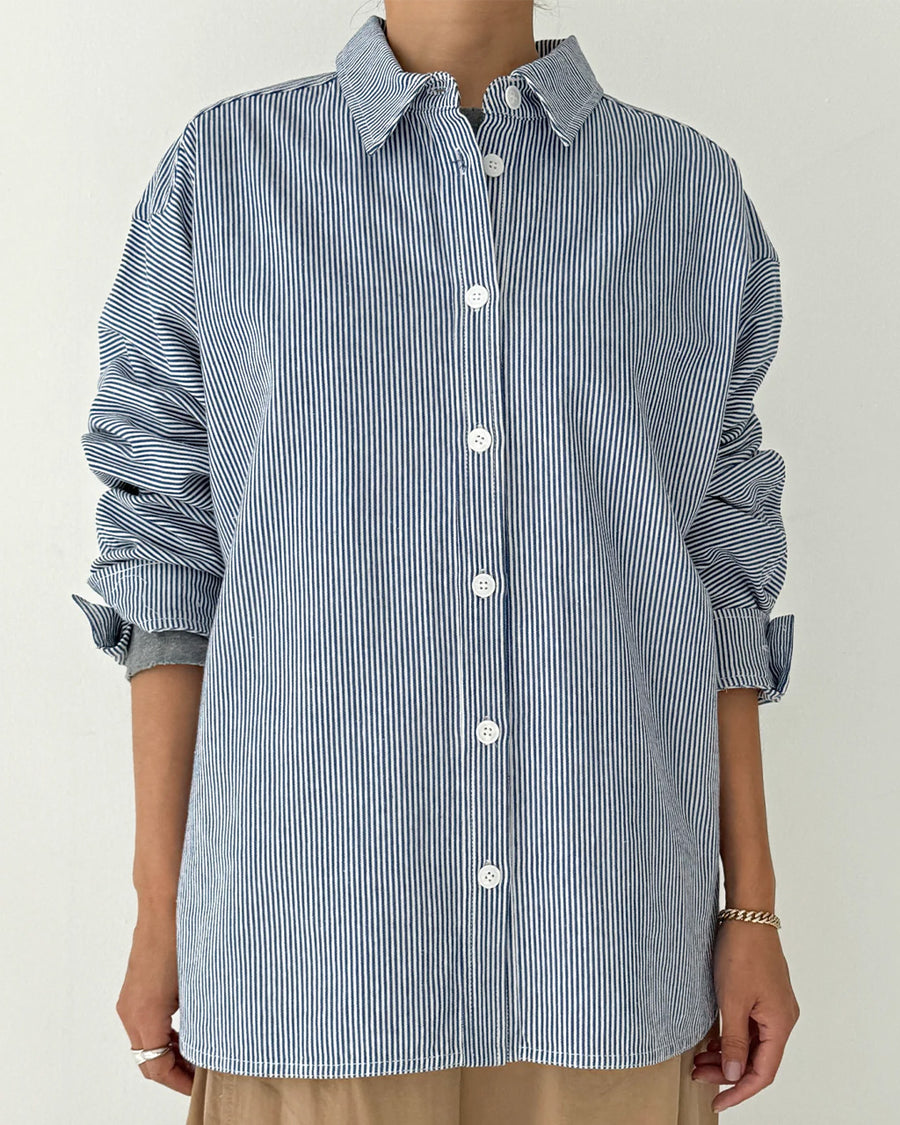 model wearing blue and white vertical pinstripe denim button up shirt