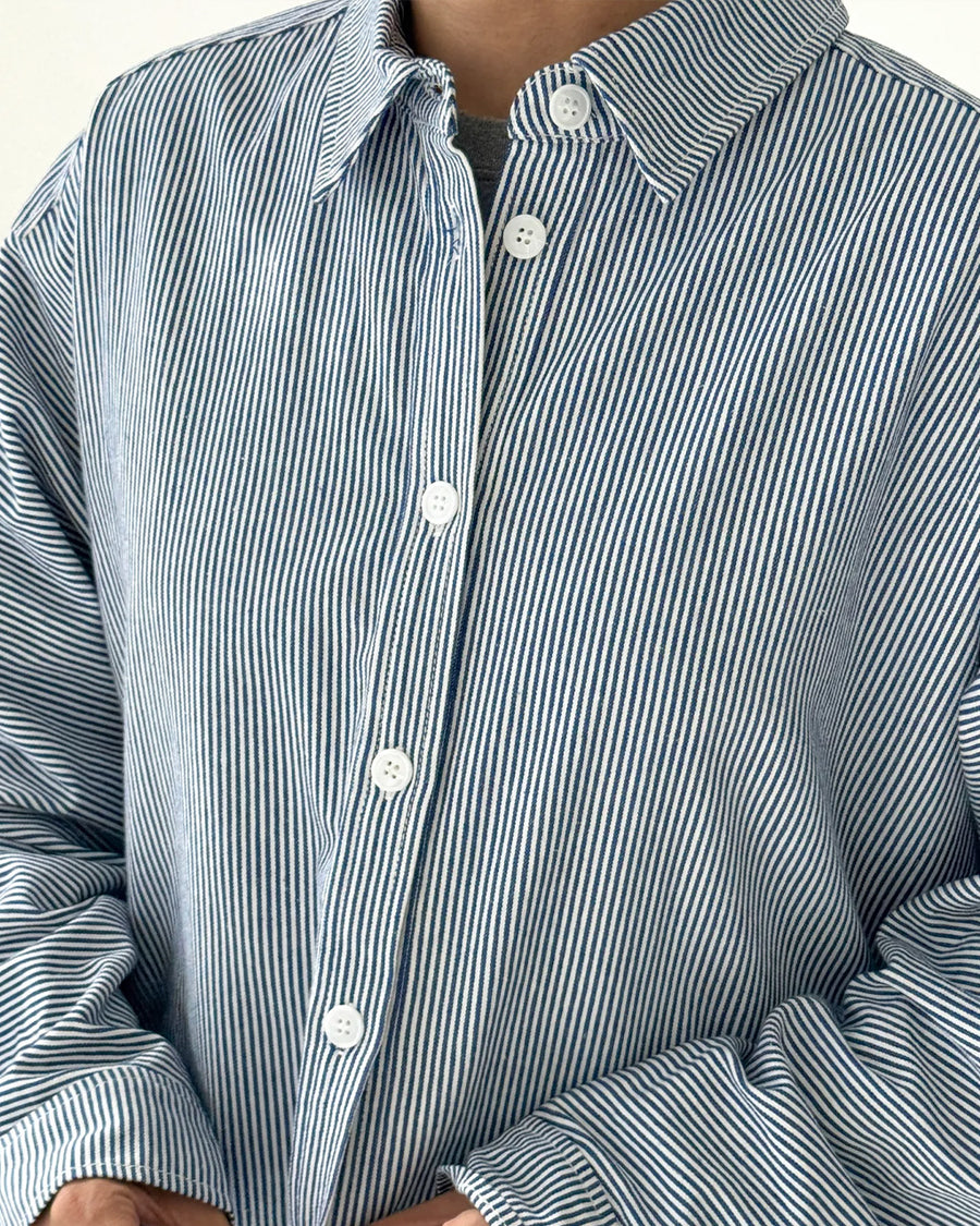 up close of model wearing blue and white vertical pinstripe denim button up shirt