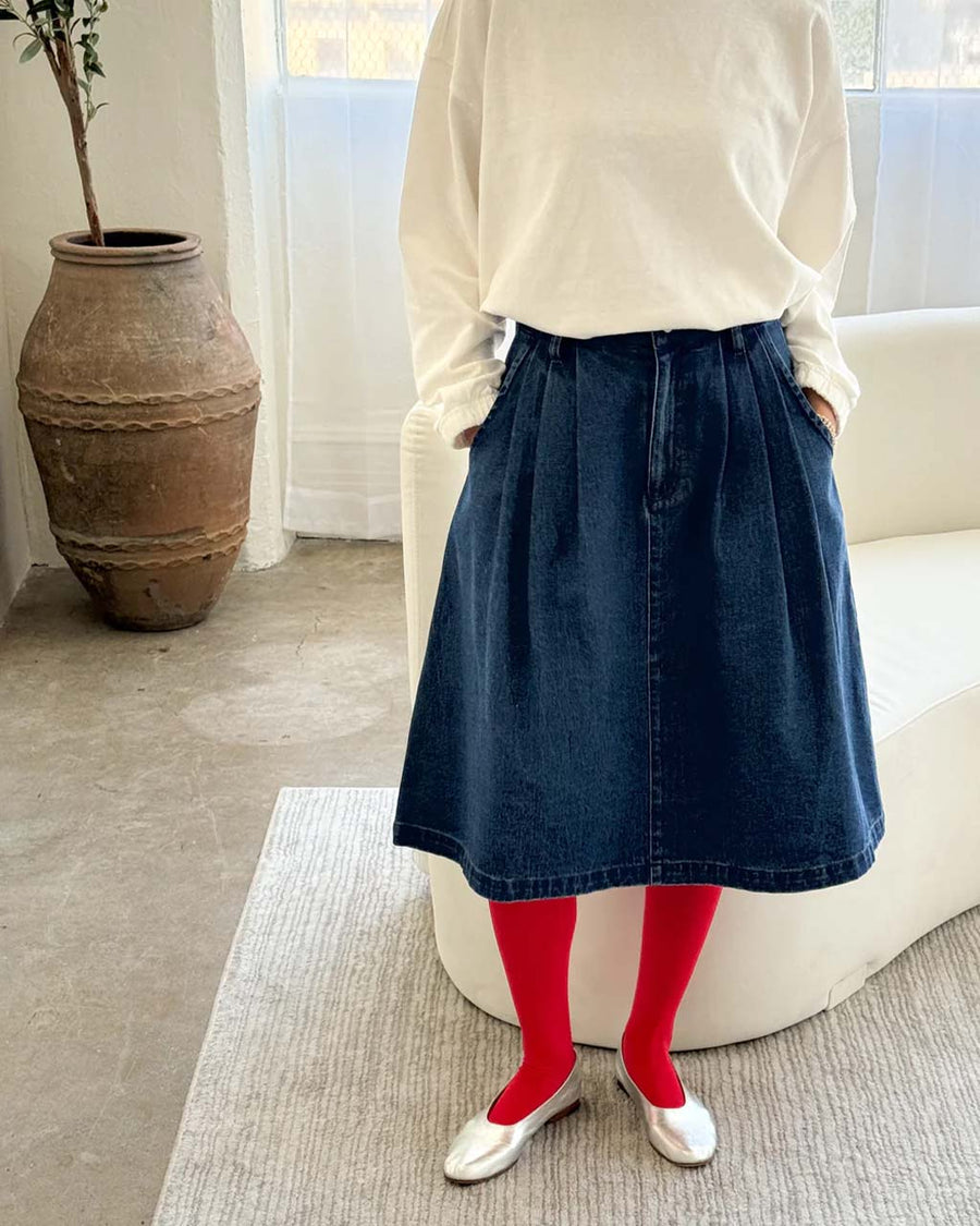 model wearing black denim midi skirt with button closure and pleated front and red tights