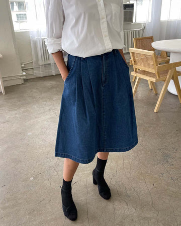 model wearing black denim midi skirt with button closure and pleated front