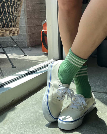 model wearing high avocado green socks with three white stripes at the top