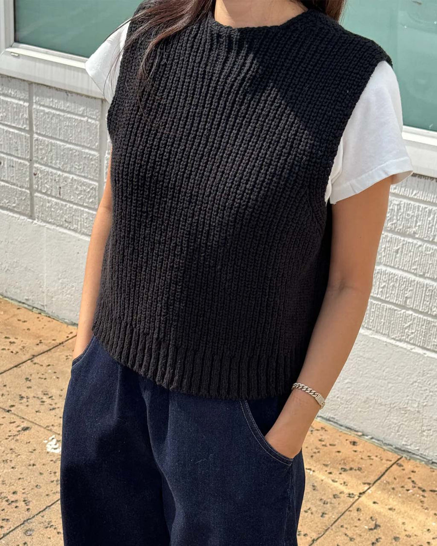 model wearing black knit open front 'granny' sweater vest backwards