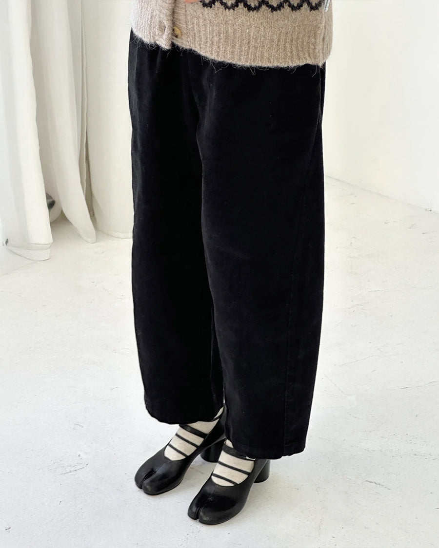 side view of model wearing black corduroy arc pants with side panels and pockets