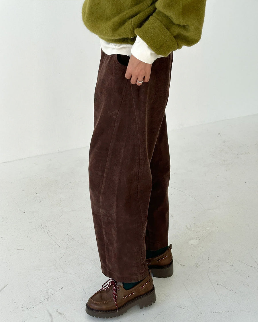 side view of model wearing chocolate brown corduroy arc pants with side panels and pockets