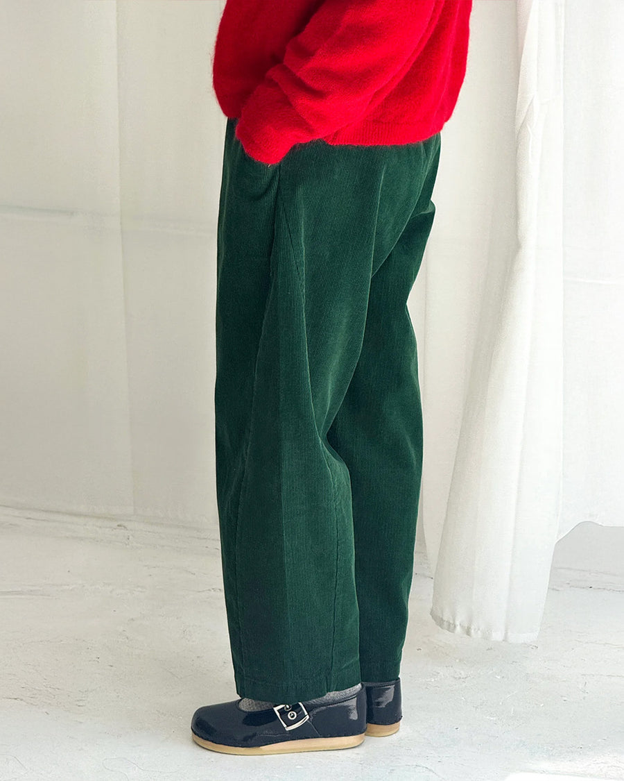side view of model wearing dark green corduroy arc pants with side panels and pockets