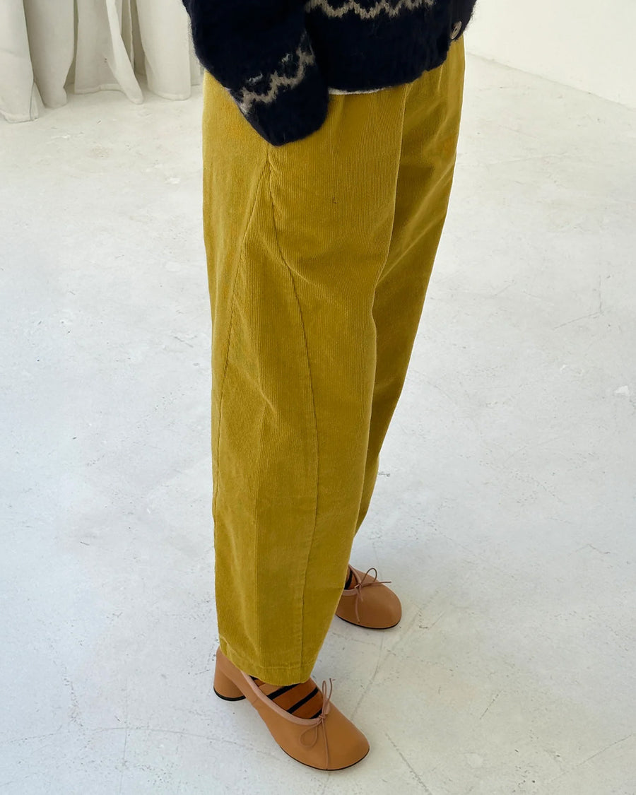 side view of model wearing green olive corduroy arc pants with side panels and pockets